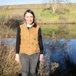 Erin Bray looking at the camera standing next to river field